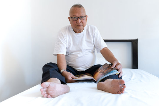 Portrait of an asian senior grases man holding a book looking at camera and he smiling on a white  bed at home.