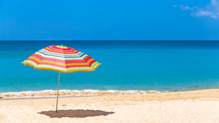 Pair of sun loungers and a beach umbrella on a deserted beach, Beach umbrella on a sunny day, sea in background.