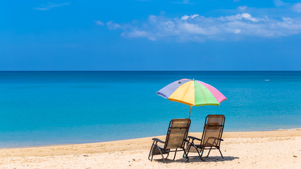 Pair of sun loungers and a beach umbrella on a deserted beach, Beach umbrella on a sunny day, sea in background.