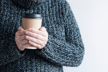 Woman holding cup of hot coffee on white wall, close up photo of hands in warm sweater with mug