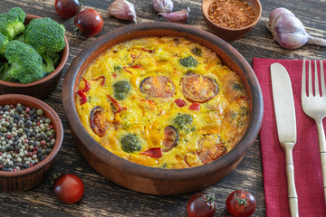 Ceramic bowl with vegetable frittata, simple vegetarian food. Frittata with egg, tomato, pepper, onion, broccoli and cheese on wooden table. Italian egg omelette