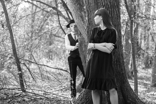 A frightened girl hides behind a tree from a masked man. The masked maniac's attack on the girl. Black and white photo. Halloween