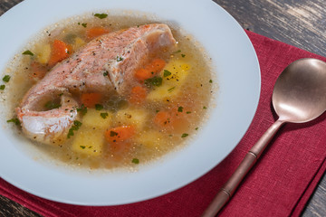Fresh salmon fish soup with carrots and potatoes in a white plate, close up