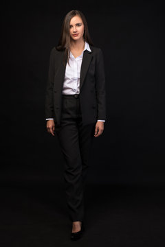 a young beautiful girl in a full-length business suit on a black background, a beautiful brunette in a jacket and black pants, long straight dark hair
