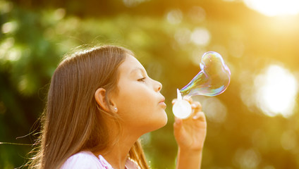 Children girl blowing soap bubbles outdoor