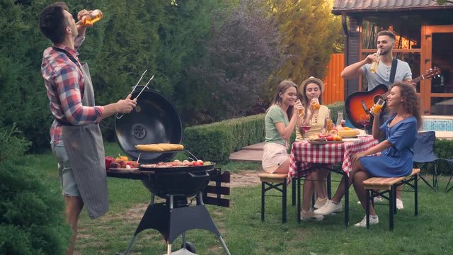 Young man cooking delicious food on grill for his friends at barbecue party outdoors. Picnic time