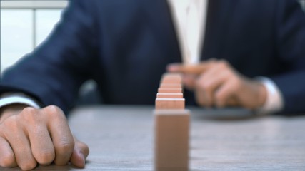 Businessman pushing domino bar causing all blocks to fall, chain reaction