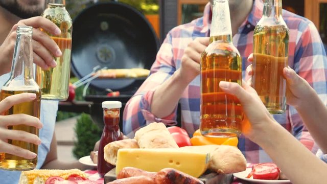 Friends clinking bottles of beer at barbecue party outdoors, closeup. Picnic time