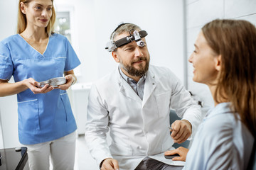 Obraz premium Patient with senior otolaryngologist and female assistant in ENT office during a medical examination