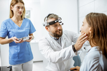 Patient with senior otolaryngologist and female assistant in ENT office during a medical examination, doctor examining nose
