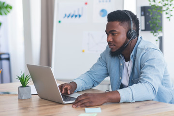 Black customer support manager with headset using laptop in office