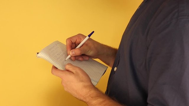 a man standing in half turn makes notes in a notebook