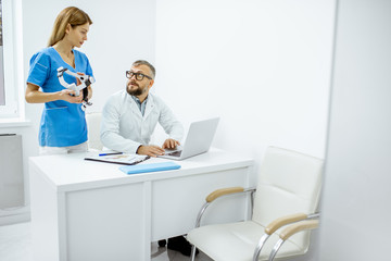 Obraz premium Senior otolaryngologist and female assistant having a medical meeting, working with laptop at the bright medical office interior