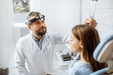 Fototapeta premium Senior otolaryngologist examining ears with ENT tuning fork for a young patient in the medical office. Hearing test with tuning fork concept