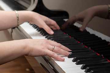 Fototapeta premium Closeup of the hands of a young woman playing the piano. The girl musician is preparing to start playing a musical composition.