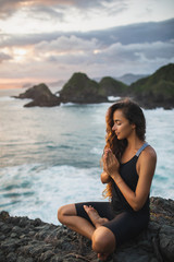 Fototapeta na wymiar Young woman praying and meditating alone at sunset with beautiful ocean and mountain view. Self-analysis and soul-searching. Spiritual and emotional concept