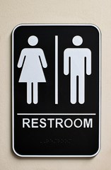 Vertical restroom sign on a wall for a unisex bathroom with male and female icons, braille at the...