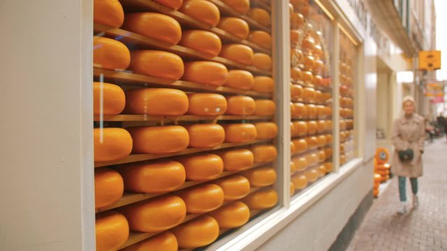 Unrecognized woman near the window of a cheese shop. A lot of rows of round cheese heads in Amsterdam, the capital of the Netherlands.
