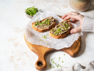 Two toasts chicken rillettes (pate) on white bread with sprouts on a wood cutting board and female...