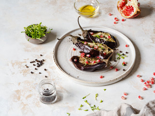 Baked eggplants slices with spices, sprouts, pomegranate and olive oil on white ceramic plate on a gray background.