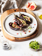 Baked eggplants slices with spices, sprouts, pomegranate and olive oil on a white ceramic plate on a gray background.