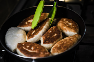 Fried pies in a pan overturn with tongs that stand on a gas stove