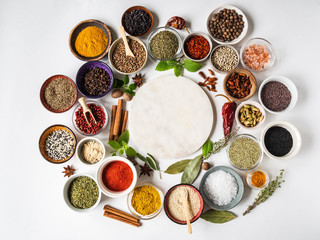Various dry spices and raw herbs frame flat lay in small bowls and wood cutting marble board in the center on white background. Top view, copy space