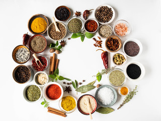 An assortment of different dry spices in small bowls and fresh herbs in the form of a circle on a white background. Top view. Copy space