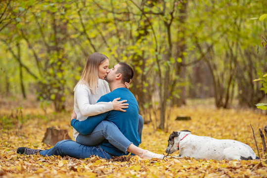 Portrait of young happy couple with cute dog kissing in autumn park