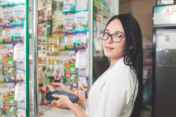 Pharmacy and the seller. A woman in glasses makes a purchase on a Bank card using a mobile terminal