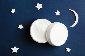 Cosmetic white container on night sky background top view. Skincare cosmetology product, night care concept. Organic cosmetics. Hand, face, body moisturizing cream jar. Women present idea