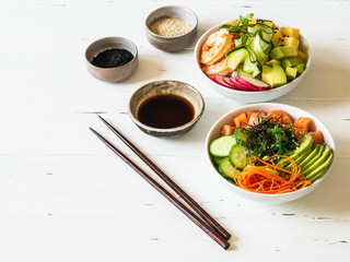 Two different Hawaiian poke bowl with seafood and fresh vegetables and fruits and rice on a white wooden background