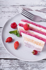 Piece of cake with many layers topped with fresh berries and mint on a ceramic plate