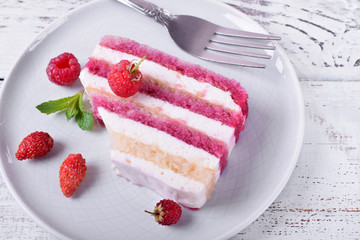 Piece of cake with many layers topped with fresh berries and mint on a ceramic plate