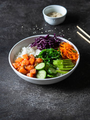 Hawaiian salmon poke bowl with rice, avocado, cucumber, carrot, red cabbage, chukka and sesame seeds on a gray background. top view