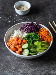 Hawaiian salmon poke bowl with rice, avocado, cucumber, carrot, red cabbage, chukka and sesame seeds on a gray background. top view
