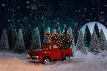 Christmas time. A toy red Chevrolet pickup truck carries a Christmas tree in the forest. The moon...