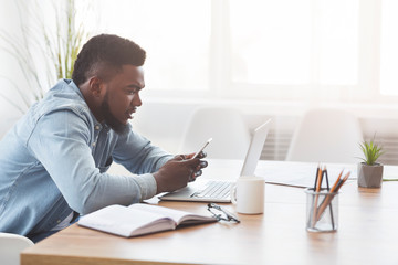 Obraz premium Black office worker using smartphone at workplace