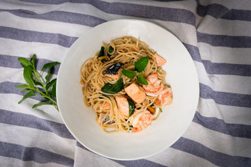 Stir-fried spaghetti with salmon, shrimp and stomach in a white bowl on a wooden table