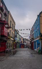 View of the main high street in Galway City with the brightly painted buildings and cobblestone streets on a cloudy day - obrazy, fototapety, plakaty