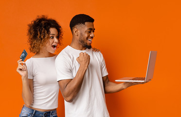 Cheerful african man and woman with credit card working on laptop