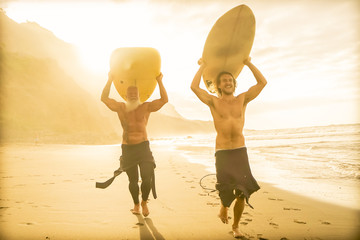 Father and son doing surfing on sunset time . Friends going out into the ocean. Sporty people...