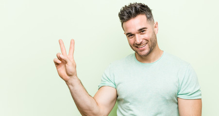 Young handsome man against a green background joyful and carefree showing a peace symbol with fingers.