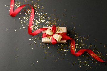 Gift or present box and gold stars confetti on black table top view. Flat lay composition for birthday, mother day, black friday sale, xmas, christmas, new year or wedding.