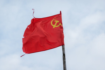 Naklejka na ściany i meble Red soviet flag on sky background with clouds. The flag has a battered appearance. There is a sign of a sickle and a hammer. Background.