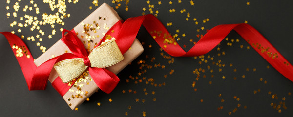 Gift or present box and gold stars confetti on black table top view. Flat lay composition for...