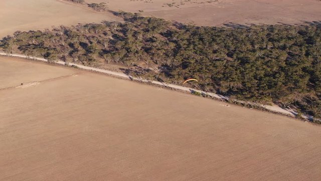 Beautiful drone aerial view of paramotor flying over the nice wide empty field at summer day