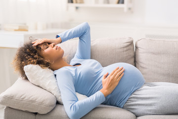 Young expectant woman with headache lying on sofa