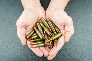 Handful of green 7.62 mm cartridges for Kalashnikov assault rifle in man's hands against a green...