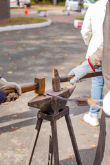 A blacksmith forges a metal blank on the anvil at a fair in the presence of spectators.